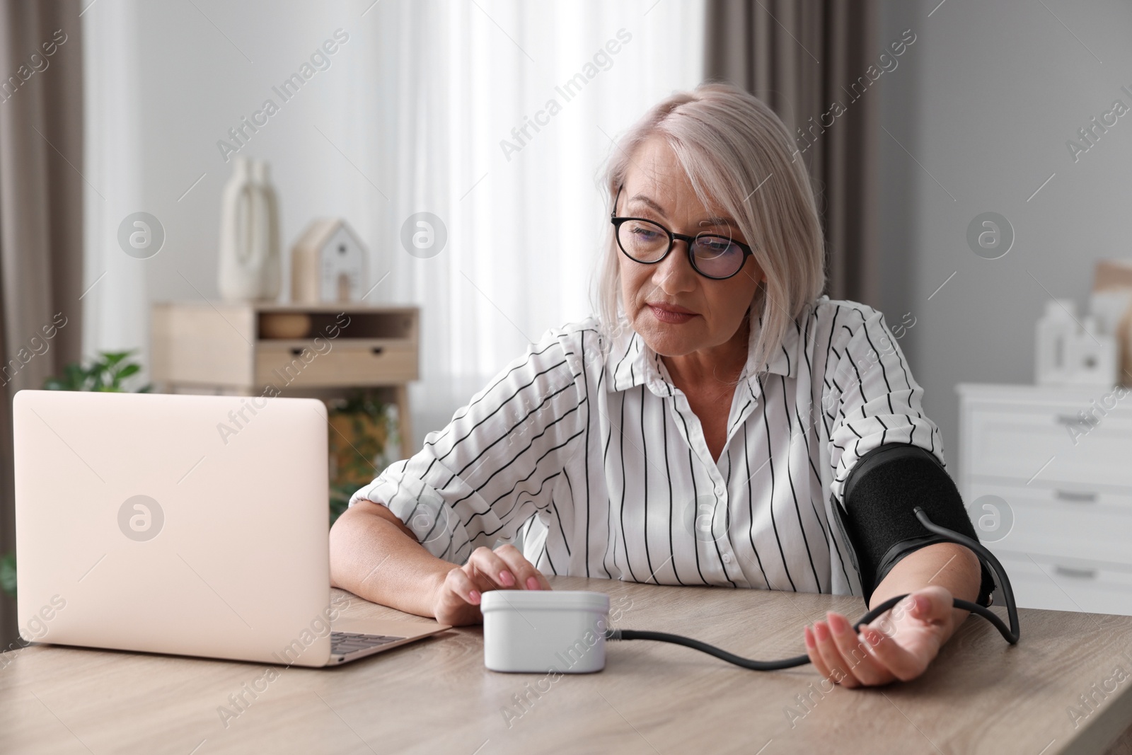 Photo of Woman measuring blood pressure at wooden table indoors