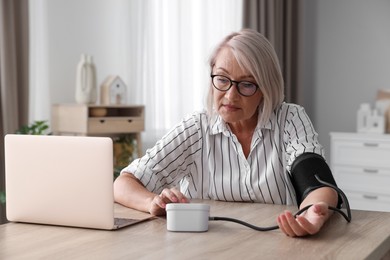 Photo of Woman measuring blood pressure at wooden table indoors