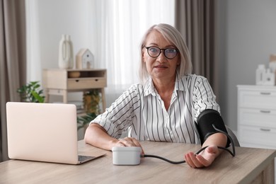 Photo of Woman measuring blood pressure at wooden table indoors