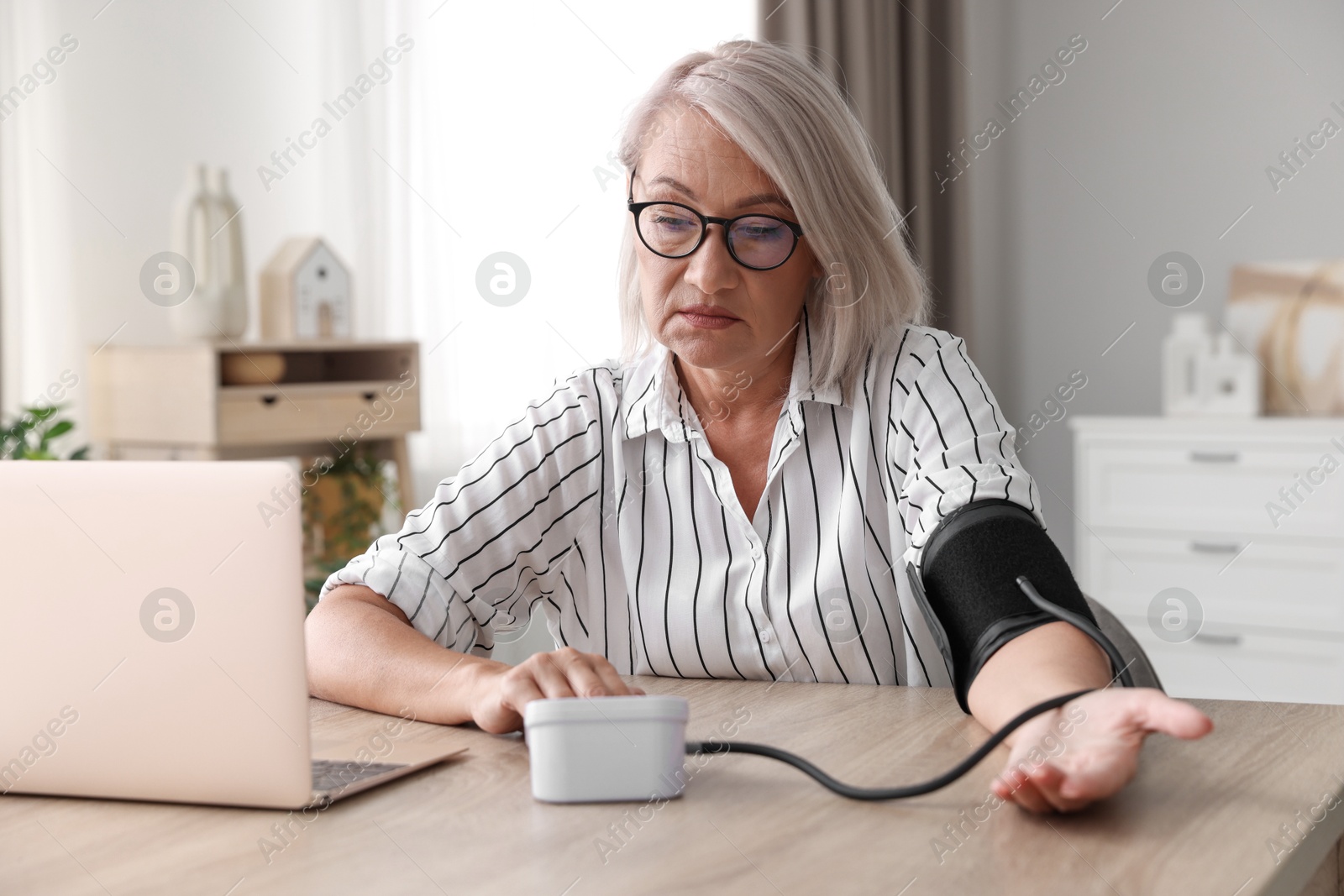 Photo of Woman measuring blood pressure at wooden table indoors