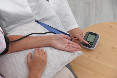 Photo of Doctor measuring patient's blood pressure at wooden table indoors, closeup