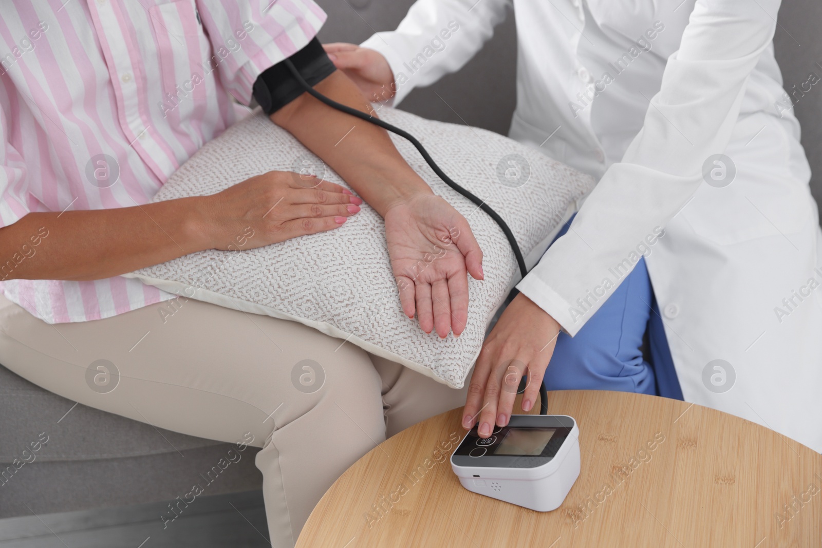 Photo of Doctor measuring patient's blood pressure on sofa indoors, closeup