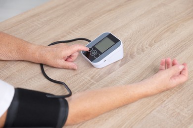 Photo of Senior woman measuring blood pressure at wooden table indoors, closeup