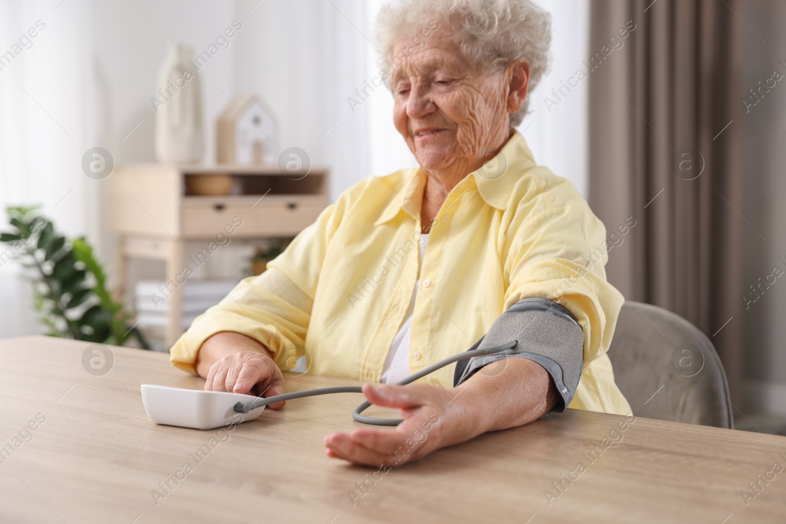 Photo of Senior woman measuring blood pressure at wooden table indoors