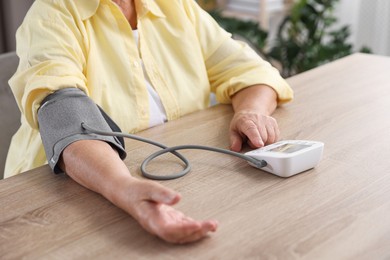 Photo of Senior woman measuring blood pressure at wooden table indoors, closeup