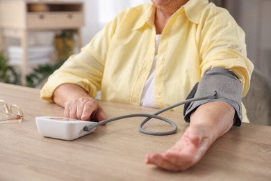 Photo of Senior woman measuring blood pressure at wooden table indoors, closeup