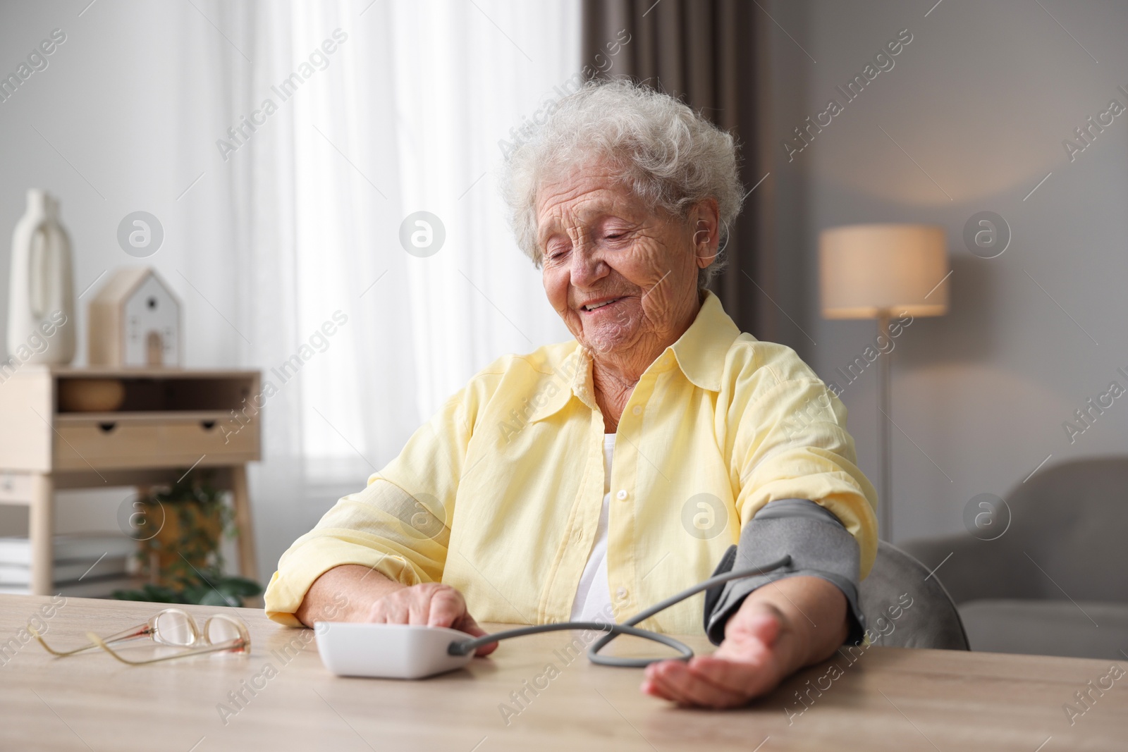 Photo of Senior woman measuring blood pressure at wooden table indoors