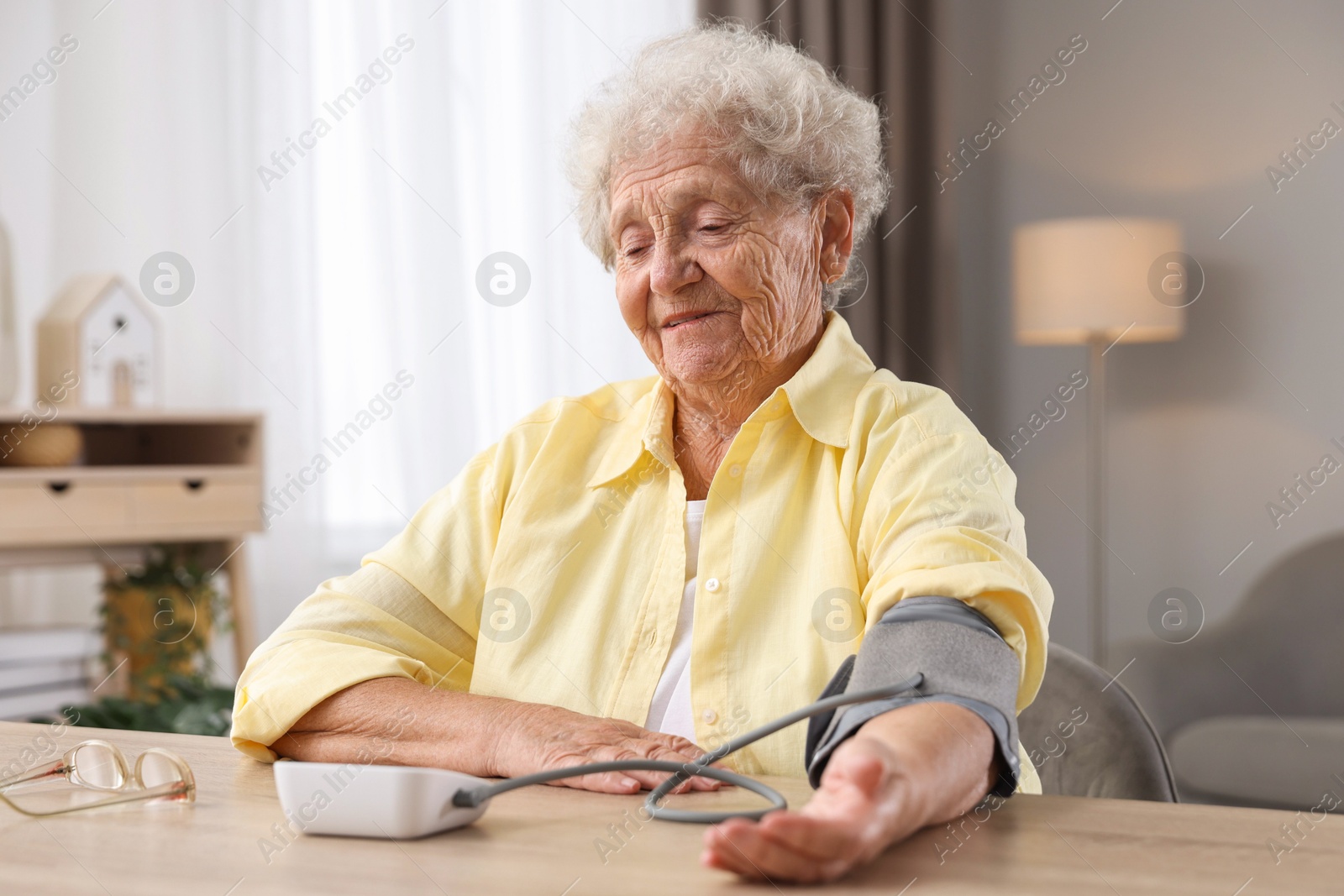 Photo of Senior woman measuring blood pressure at wooden table indoors