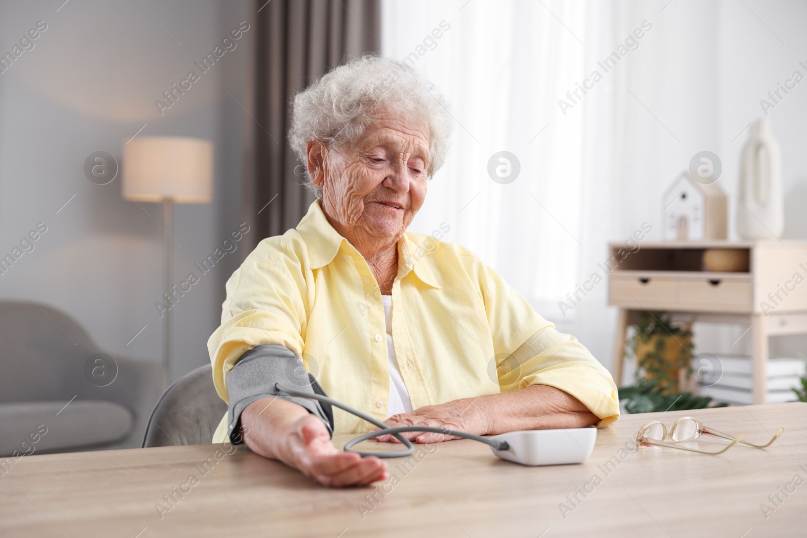 Photo of Senior woman measuring blood pressure at wooden table indoors