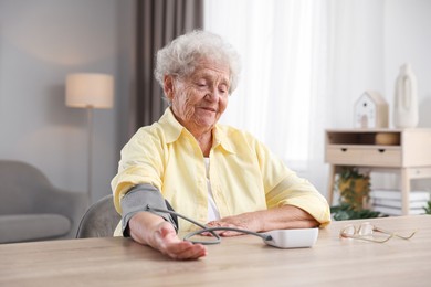 Photo of Senior woman measuring blood pressure at wooden table indoors