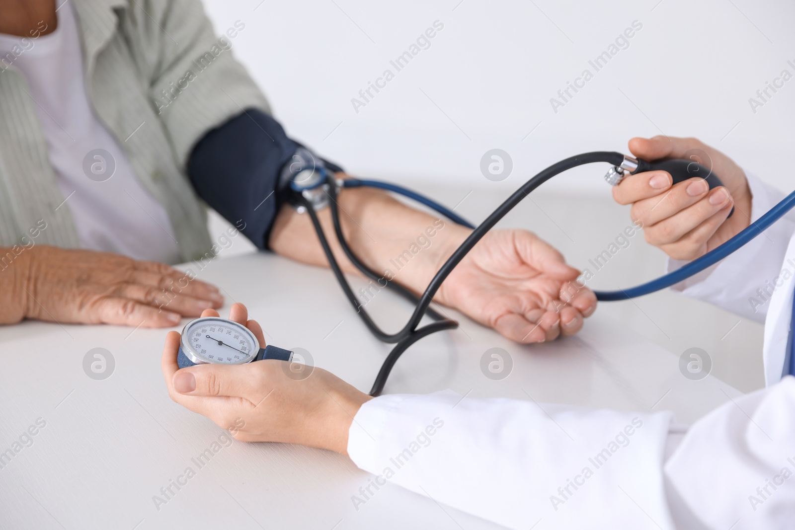 Photo of Doctor measuring patient's blood pressure at table in hospital, closeup