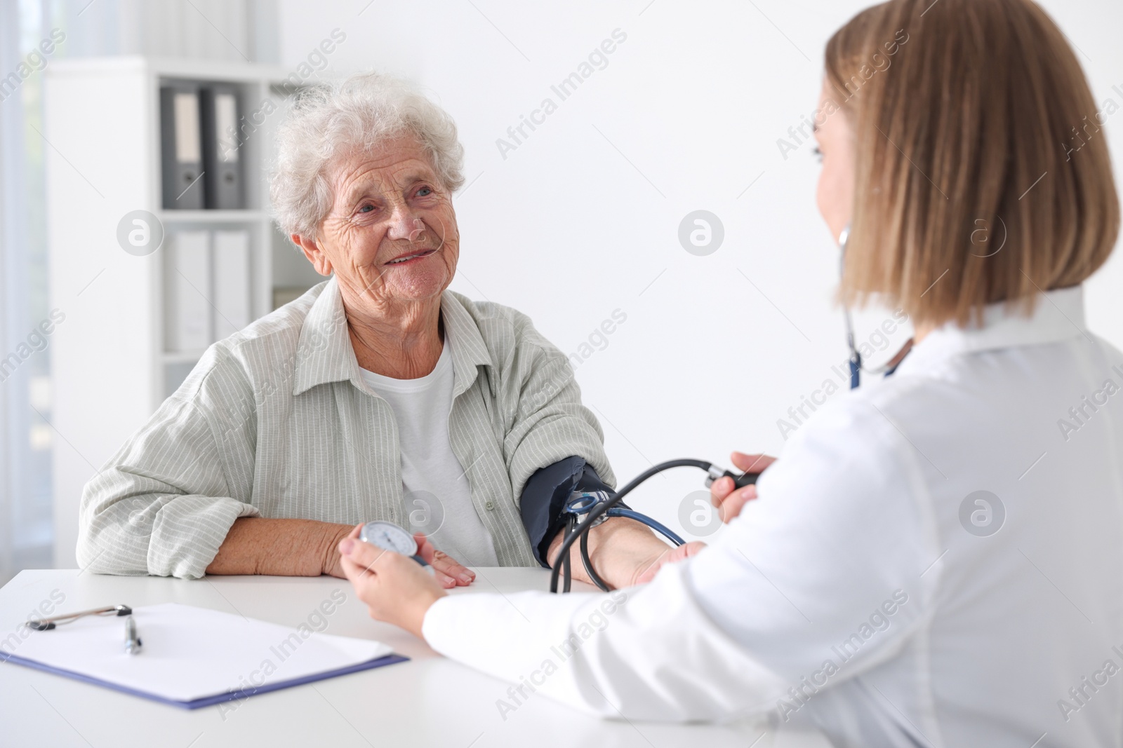 Photo of Doctor measuring patient's blood pressure at table in hospital