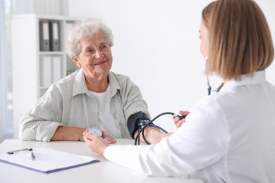 Photo of Doctor measuring patient's blood pressure at table in hospital