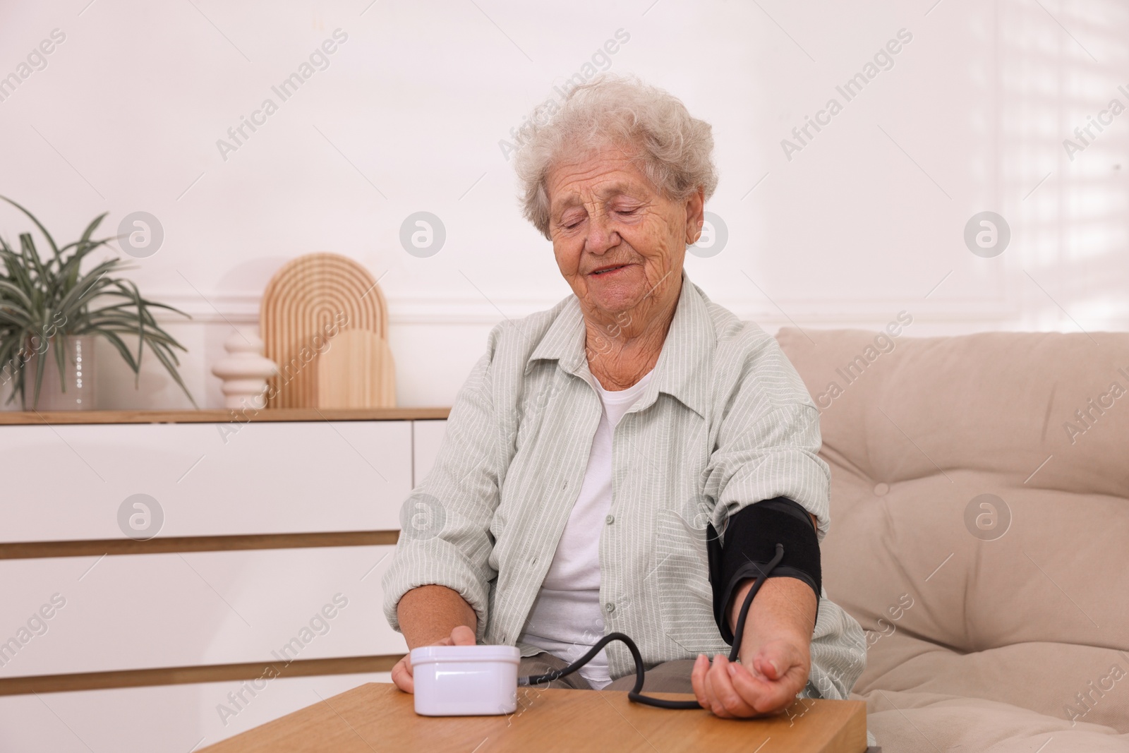 Photo of Senior woman measuring blood pressure at wooden table indoors