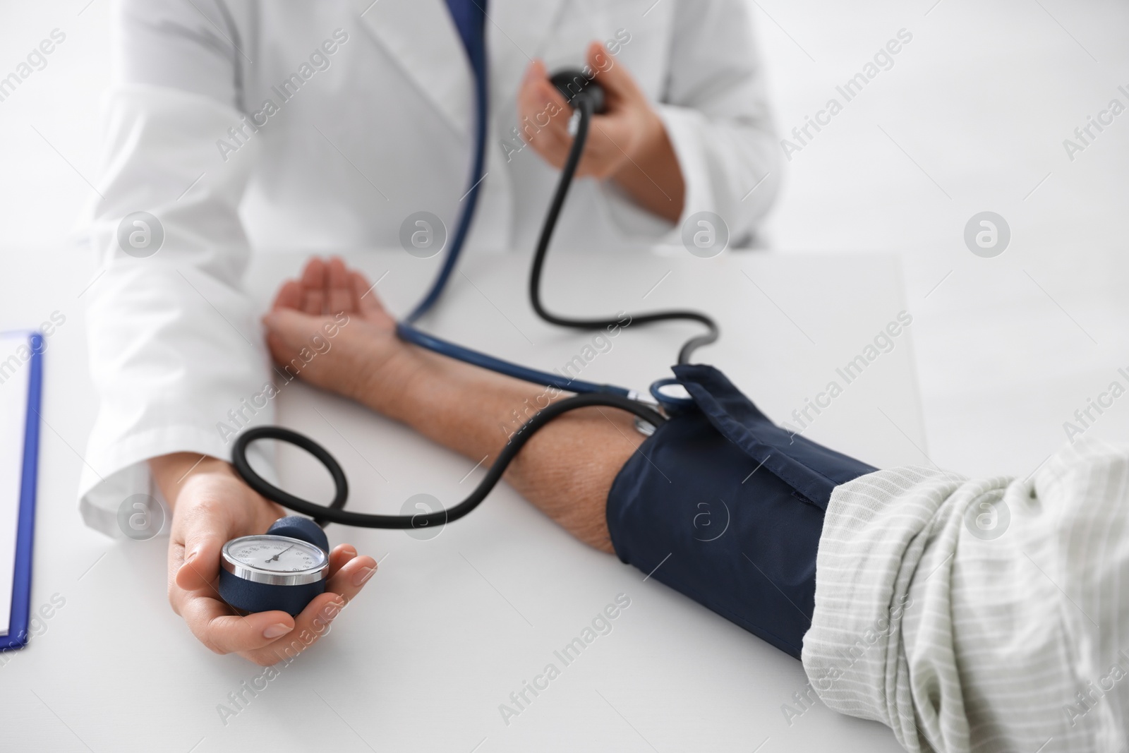 Photo of Doctor measuring patient's blood pressure at table in hospital, closeup