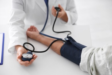 Photo of Doctor measuring patient's blood pressure at table in hospital, closeup