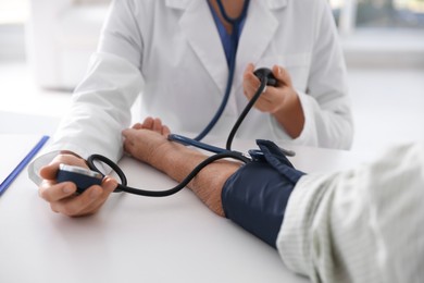 Photo of Doctor measuring patient's blood pressure at table in hospital, closeup