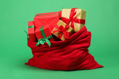 Photo of Red Santa Claus bag with gift boxes on green background