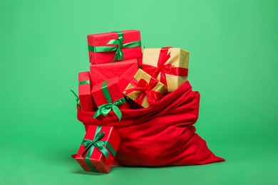 Photo of Red Santa Claus bag with gift boxes on green background