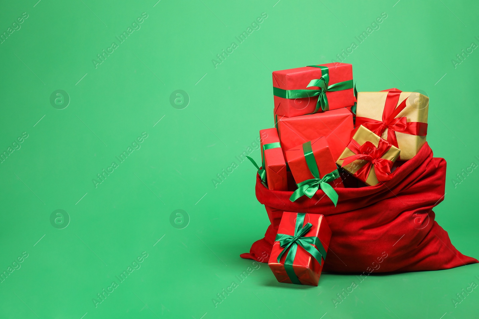 Photo of Red Santa Claus bag with gift boxes on green background, space for text