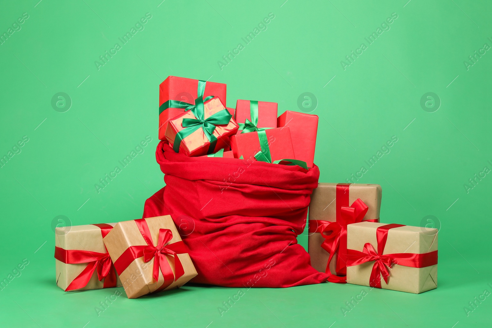 Photo of Red Santa Claus bag with gift boxes on green background