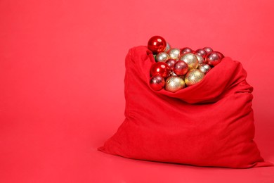 Photo of Santa bag with baubles on red background, space for text