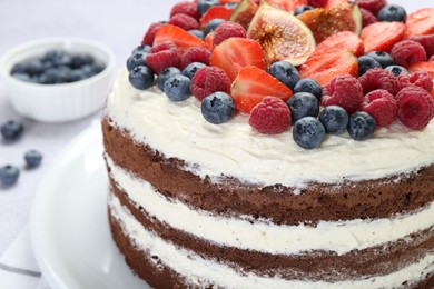 Delicious chocolate sponge cake with berries on light table, closeup