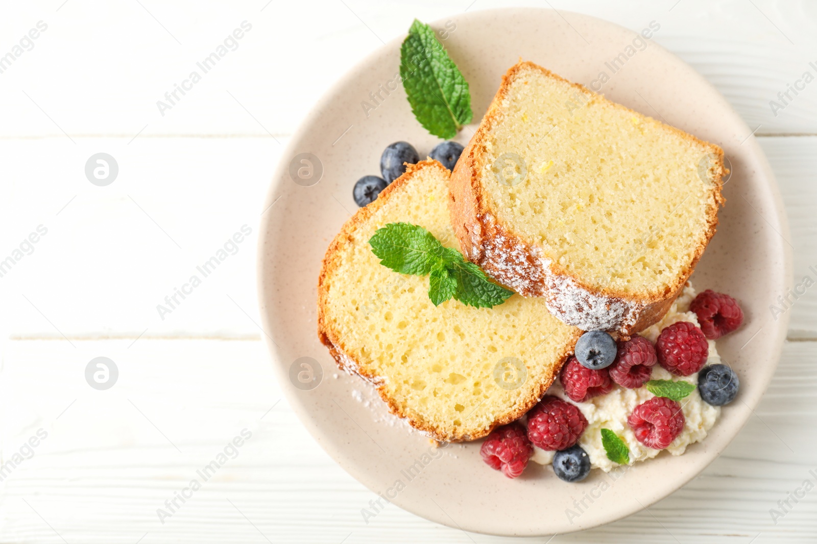 Photo of Freshly baked sponge cake, whipped cream, berries and mint on white wooden table, top view. Space for text