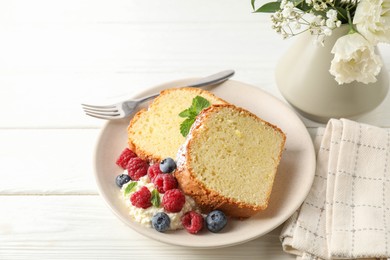 Photo of Freshly baked sponge cake, whipped cream, berries and mint on white wooden table