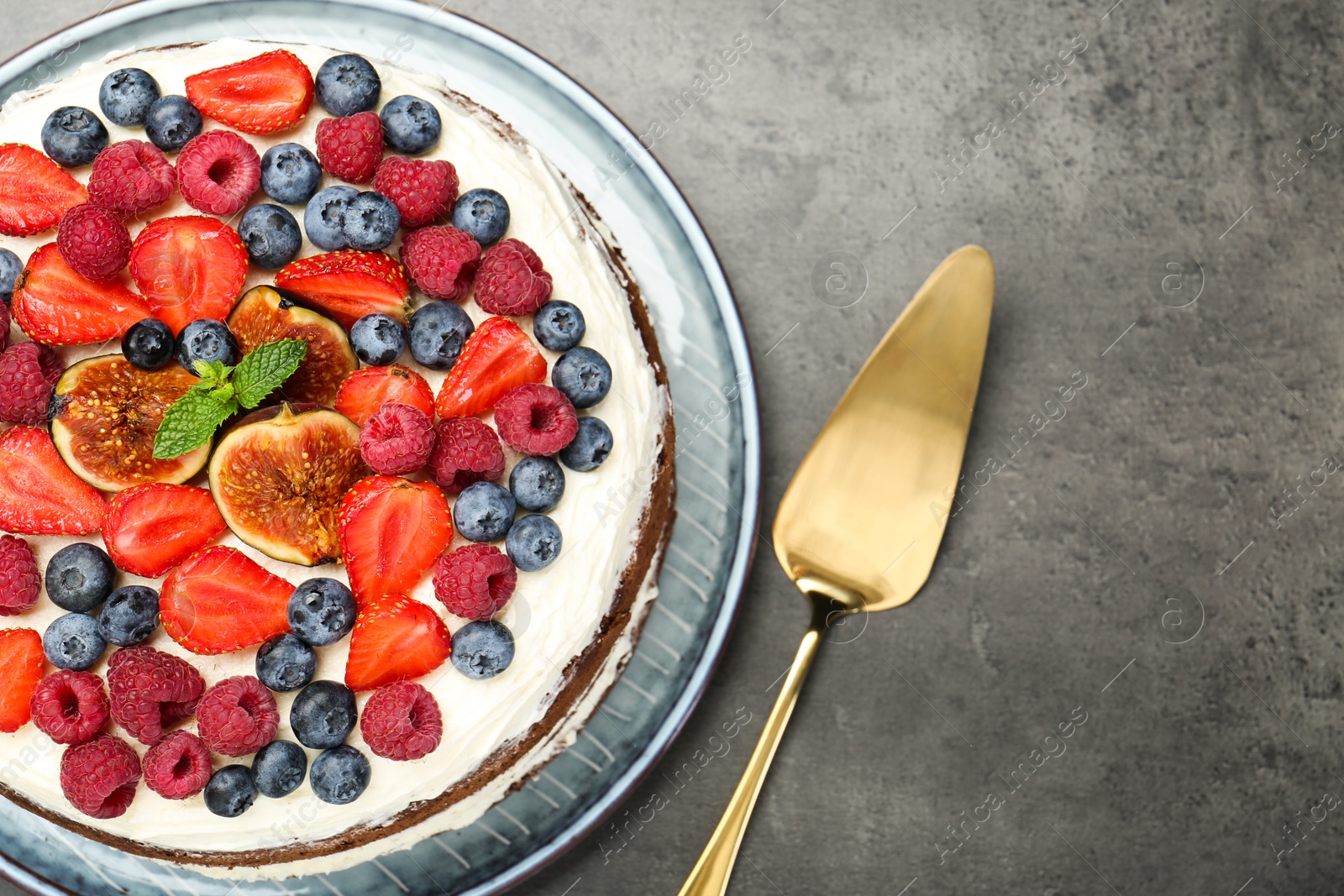 Photo of Delicious chocolate sponge cake with berries and server on grey table, top view