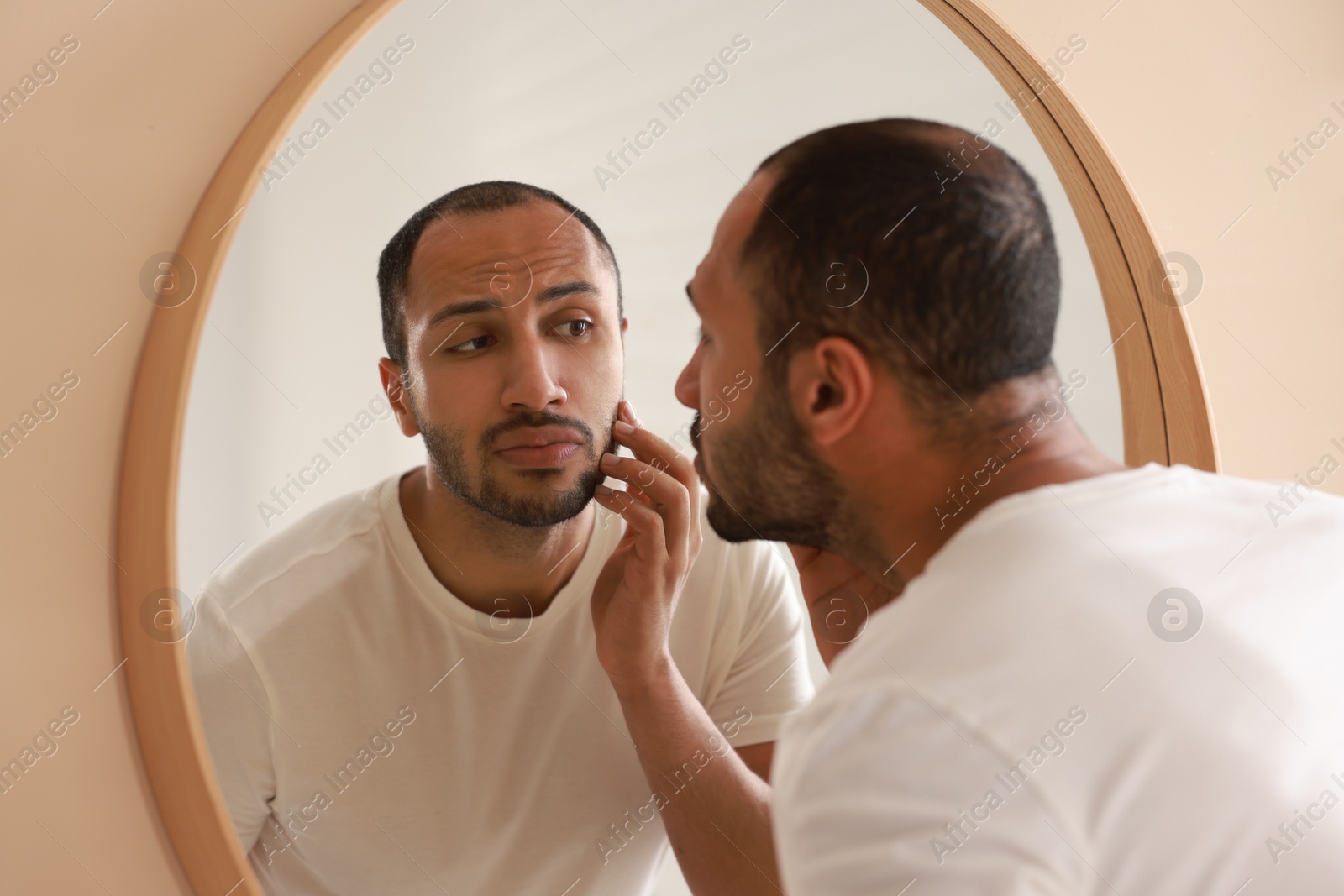 Photo of Worried man looking at mirror in bathroom