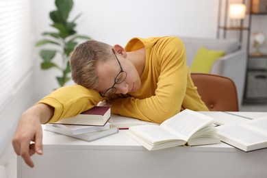 Photo of Preparing for exam. Tired student sleeping among books at table indoors