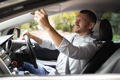 Photo of Man adjusting rear-view mirror in car before driving