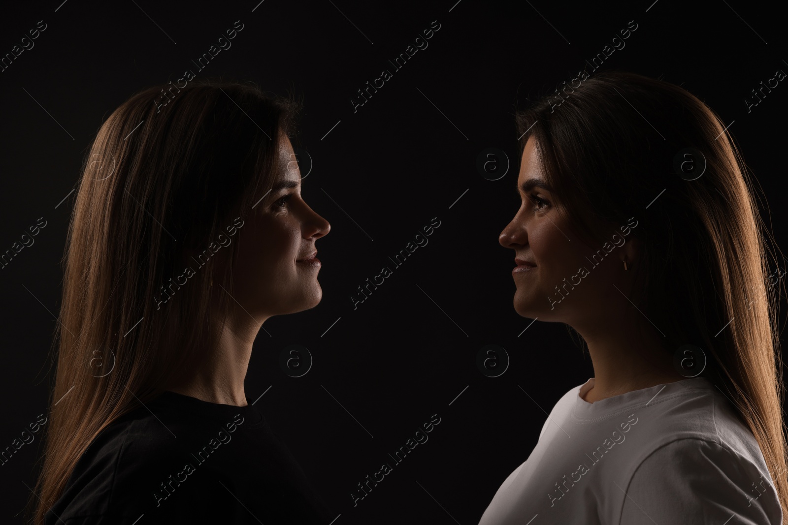 Photo of Portrait of beautiful twin sisters on black background