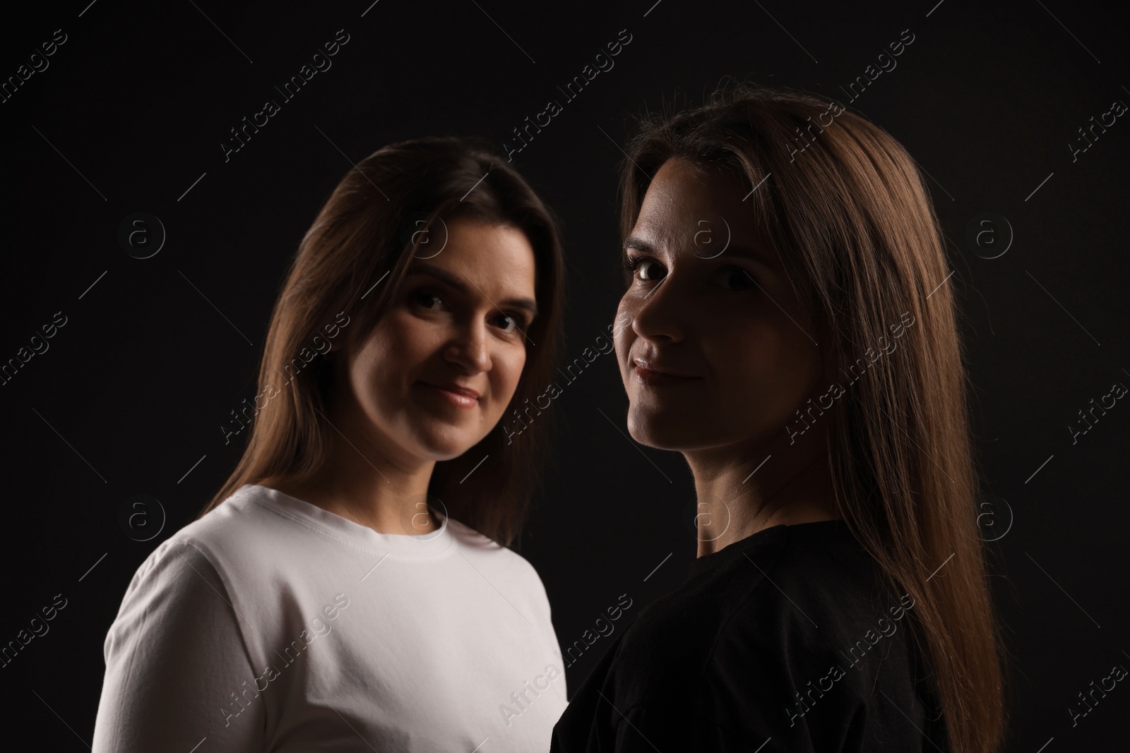 Photo of Portrait of beautiful twin sisters on black background