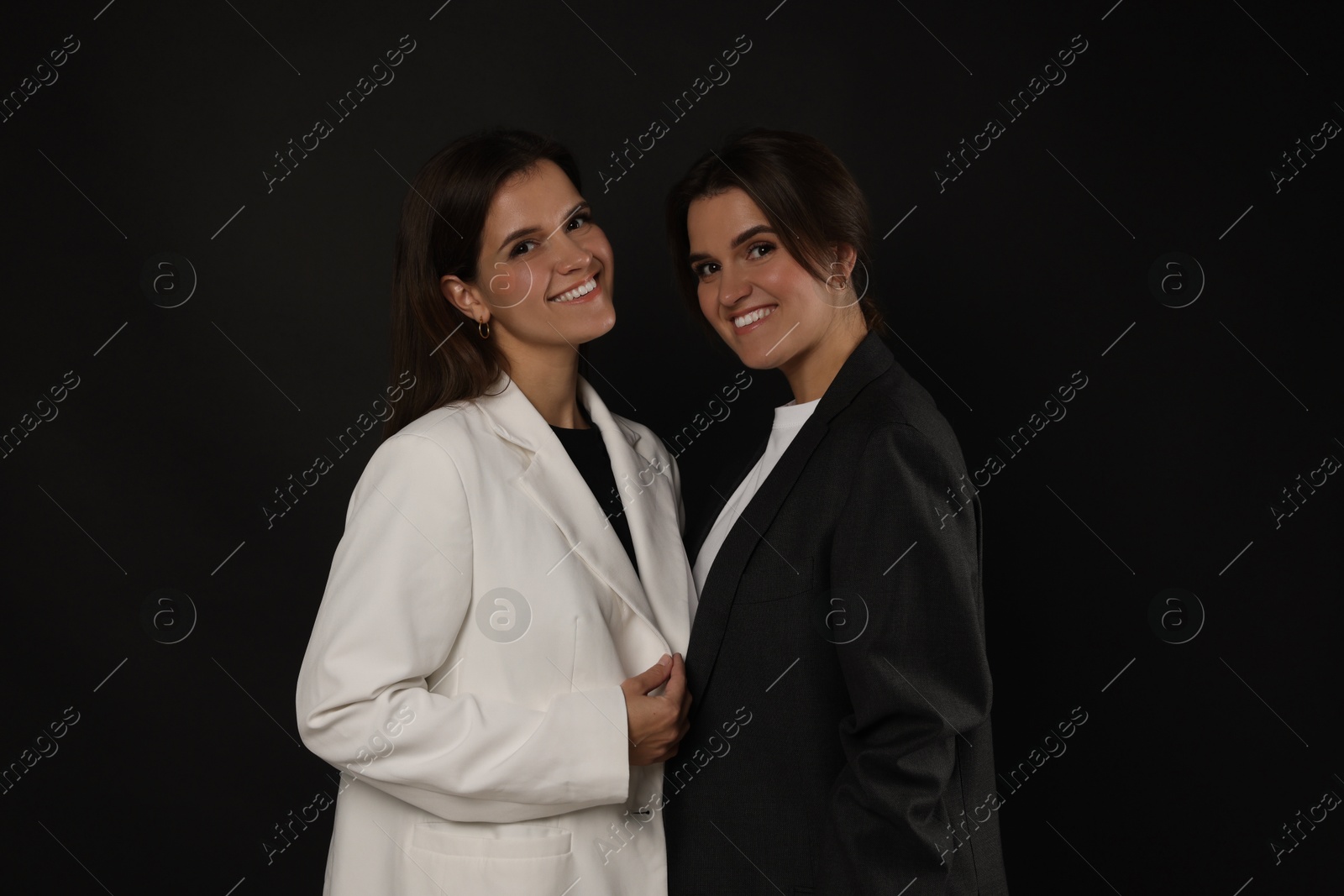 Photo of Portrait of beautiful twin sisters on black background