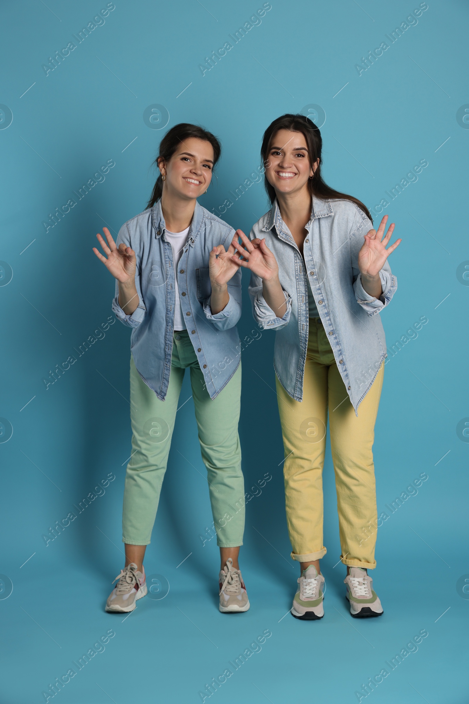 Photo of Beautiful twin sisters showing ok gestures on light blue background