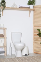 Photo of Folding screen, toilet bowl and houseplants in restroom. Interior design