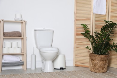 Photo of Folding screen, toilet bowl and houseplant in restroom. Interior design