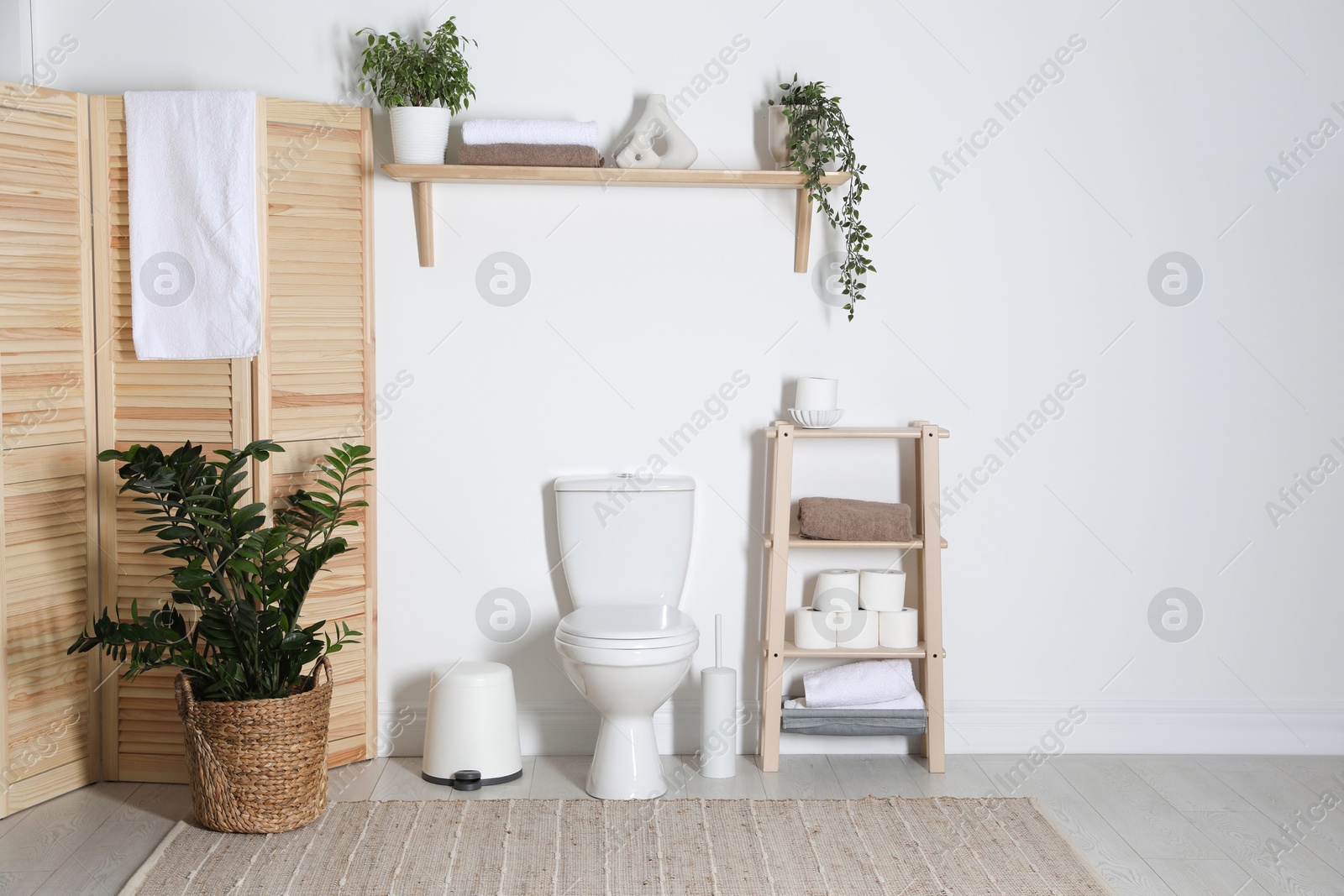 Photo of Stylish restroom interior with folding screen, toilet bowl and houseplant