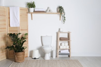 Photo of Stylish restroom interior with folding screen, toilet bowl and houseplant