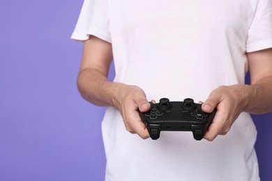 Photo of Man playing video games with controller on violet background, closeup. Space for text