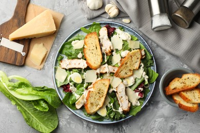 Tasty Caesar salad with chicken and ingredients on gray textured table, flat lay