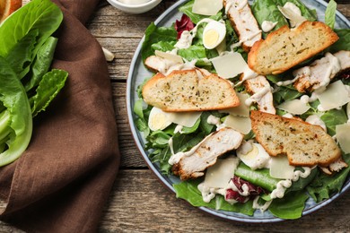 Photo of Tasty Caesar salad with chicken on wooden table, flat lay