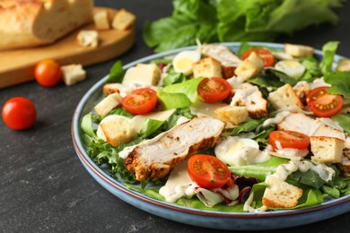 Photo of Tasty Caesar salad with chicken and tomatoes on dark gray textured table, closeup