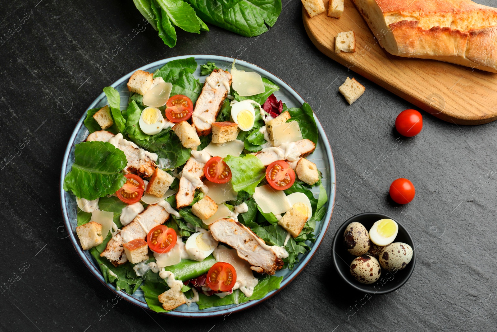 Photo of Tasty Caesar salad with chicken and ingredients on dark gray textured table, flat lay