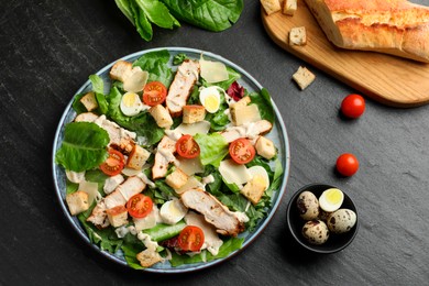 Photo of Tasty Caesar salad with chicken and ingredients on dark gray textured table, flat lay