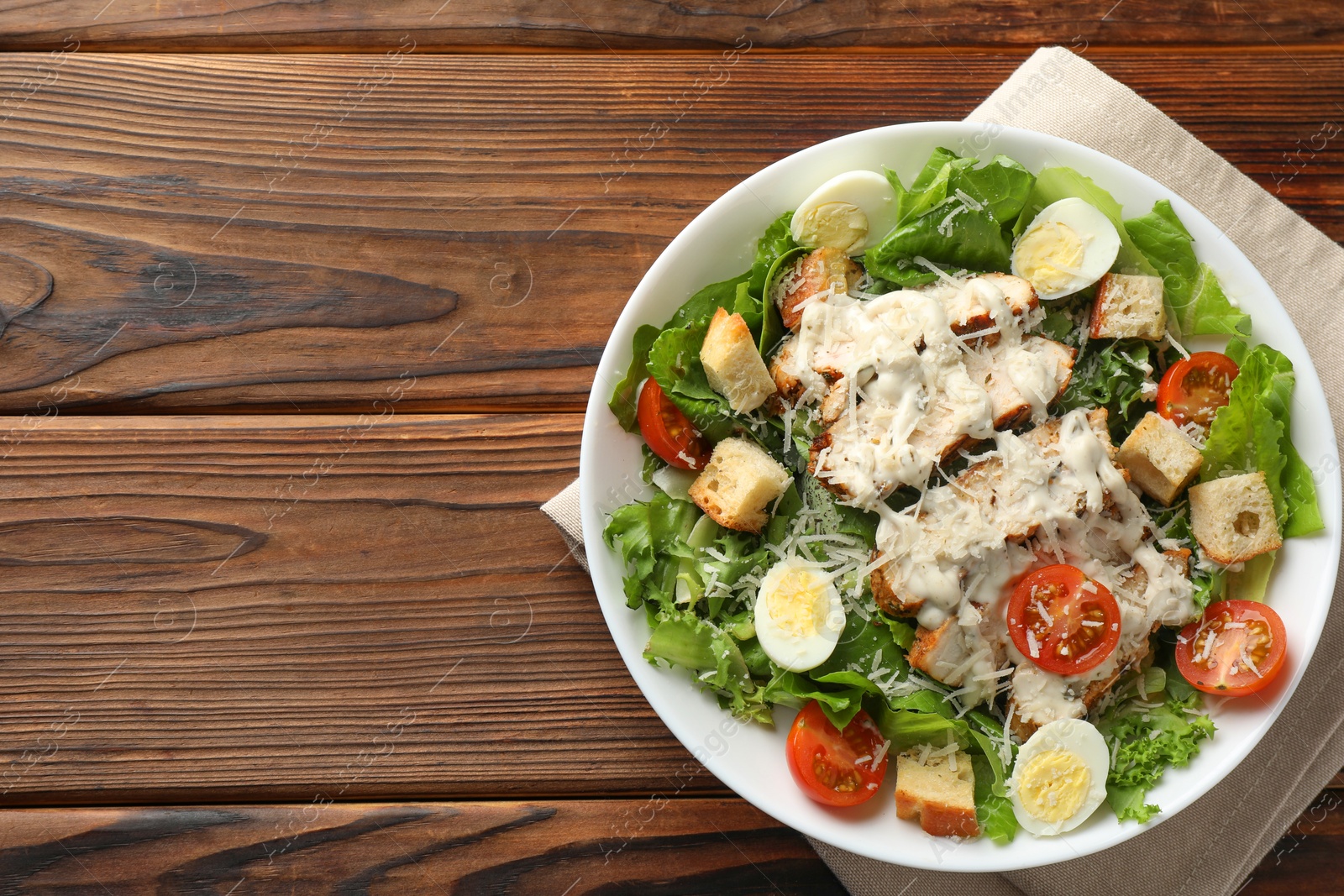 Photo of Tasty Caesar salad with chicken and tomatoes in bowl on wooden table, top view. Space for text