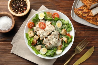 Photo of Tasty Caesar salad with chicken and tomatoes in bowl served on wooden table, flat lay