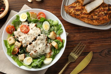 Photo of Tasty Caesar salad with chicken and tomatoes in bowl served on wooden table, flat lay